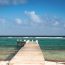 Rustic wooden pier with white posts extending into turquoise Caribbean water in the Cayman Islands with waves breaking on the reef in the distance