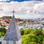 Panoramic view of Gustavia harbor in St. Barts with a church steeple in the foreground, colorful buildings on hillsides, and yachts anchored in the turquoise bay
