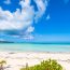 Pristine white sand beach in Turks and Caicos with stunning turquoise water, blue sky with white clouds, and lush vegetation along the shoreline