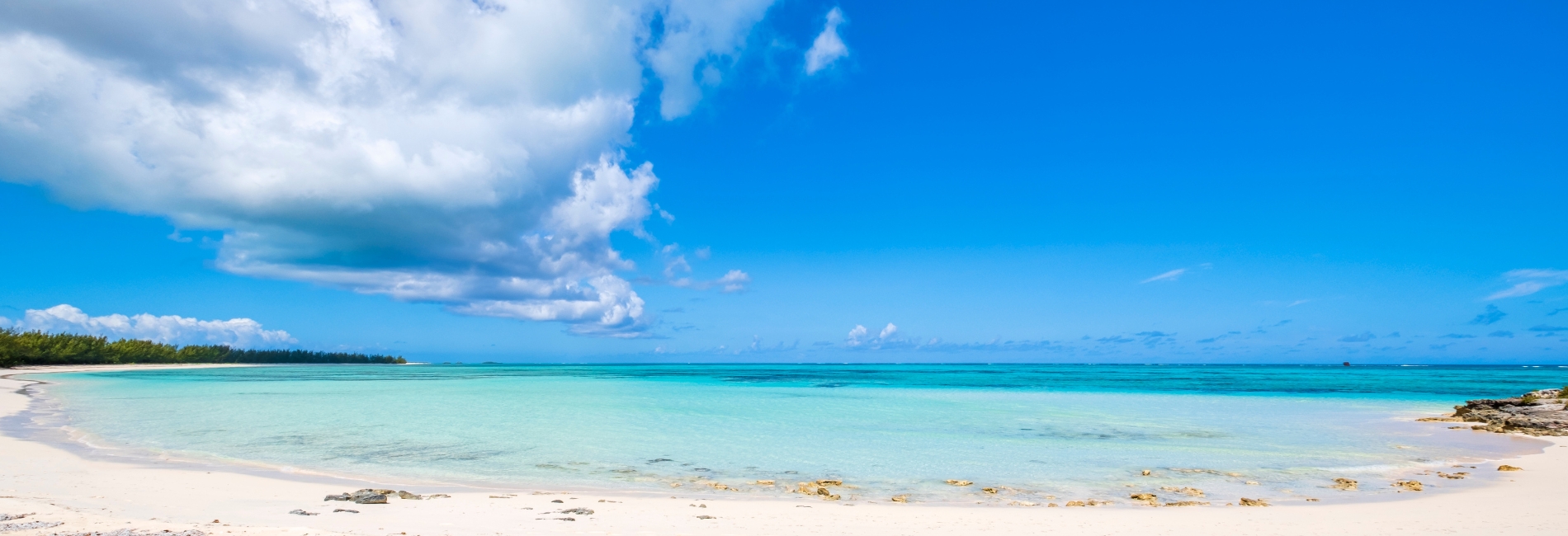 Pristine white sand beach in Turks and Caicos with stunning turquoise water, blue sky with white clouds, and lush vegetation along the shoreline