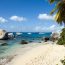 Scenic beach in the U.S. Virgin Islands with large granite boulders, clear turquoise water, anchored sailboats, and palm trees