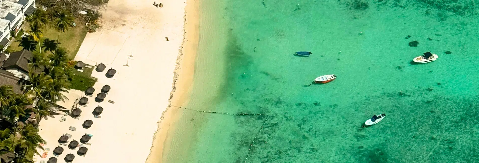 Bimini, Bahamas Beach Resort with White Sand and Crystal Clear Water Aerial view of a pristine white sand beach in Bimini with rows of beach umbrellas, palm trees, and boats anchored in crystal clear turquoise water