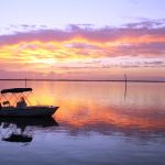 Stunning sunset in Spanish Wells, Bahamas with a small boat silhouetted against pink and orange sky reflecting on calm water
