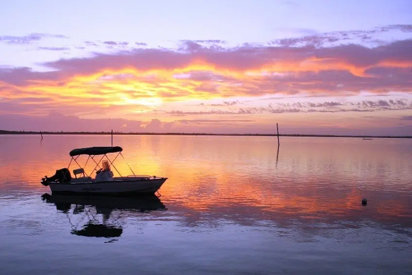 Stunning sunset in Spanish Wells, Bahamas with a small boat silhouetted against pink and orange sky reflecting on calm water