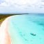 Harbour Island's famous pink sand beach with crystal clear turquoise water, swimmers, and a boat floating in the shallow bay