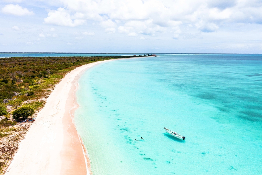 Harbour Island's famous pink sand beach with crystal clear turquoise water, swimmers, and a boat floating in the shallow bay