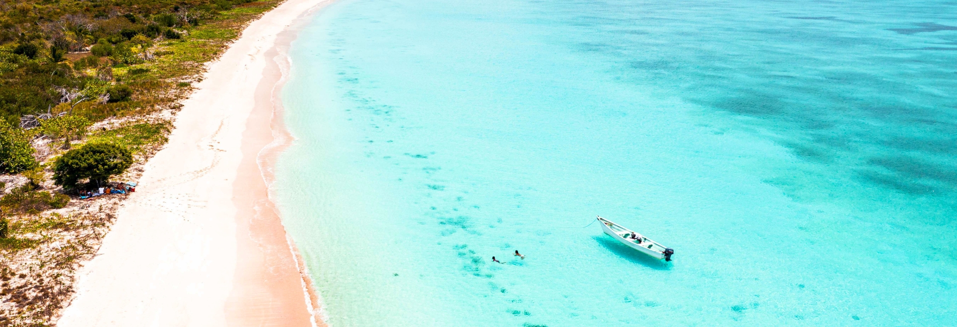 Harbour Island's famous pink sand beach with crystal clear turquoise water, swimmers, and a boat floating in the shallow bay