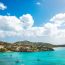 Stunning turquoise bay in Antigua with sailboats anchored in crystal clear water, green hillsides dotted with white homes, and scenic beaches along the coastline