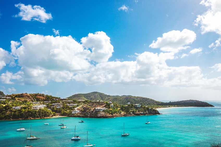 Stunning turquoise bay in Antigua with sailboats anchored in crystal clear water, green hillsides dotted with white homes, and scenic beaches along the coastline