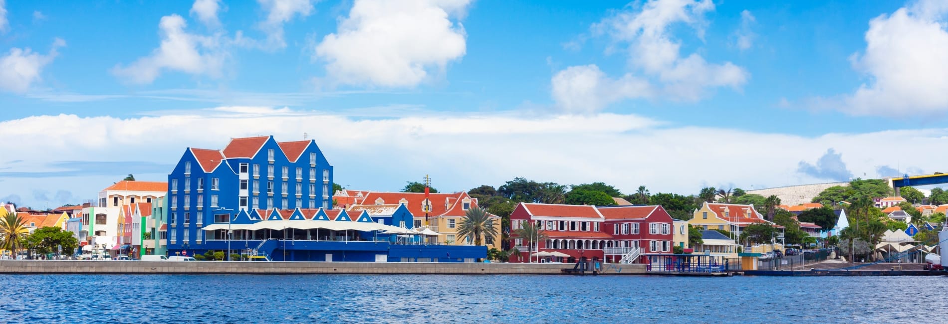 Colorful Dutch colonial buildings along the Willemstad waterfront in Curacao featuring palm trees, and vibrant architecture