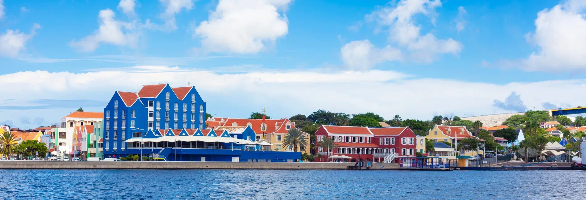 Colorful Dutch colonial buildings along the Willemstad waterfront in Curacao featuring palm trees, and vibrant architecture