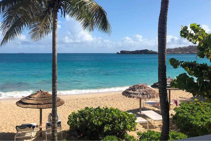 Beautiful beach at Galley Bay all-inclusive resort in Antigua with golden sand, thatched palapa umbrellas, palm trees, beach loungers, and turquoise Caribbean water