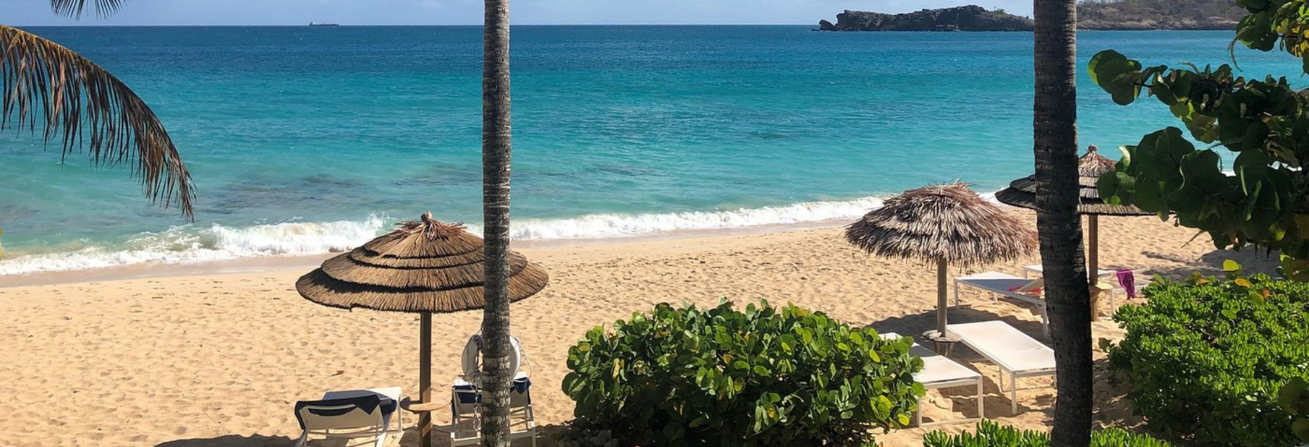 Beautiful beach at Galley Bay all-inclusive resort in Antigua with golden sand, thatched palapa umbrellas, palm trees, beach loungers, and turquoise Caribbean water