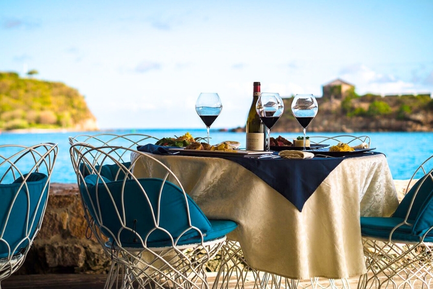 Romantic fine dining setup at Incanto Restaurant and Lounge Bar in Antigua featuring wine bottle, elegant table setting, fresh cuisine, and scenic ocean and hillside views