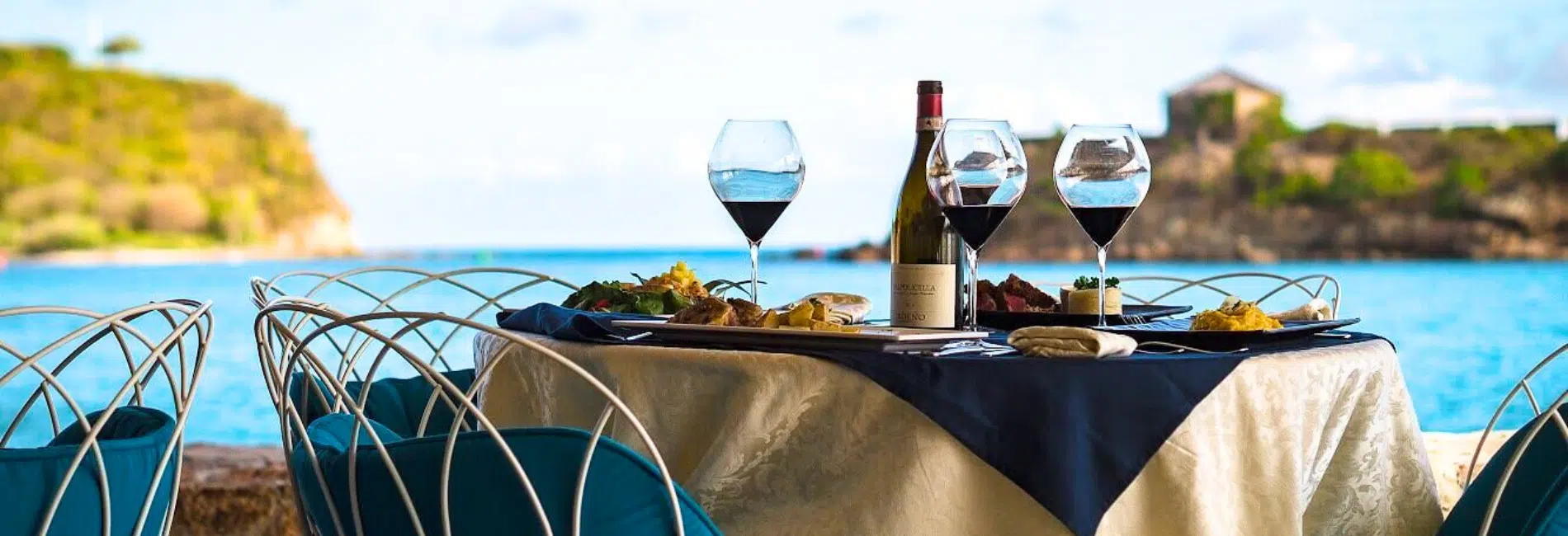 Incanto Restaurant and Lounge Bar, Antigua Oceanfront Dining Elegant oceanfront dining table at Incanto Restaurant and Lounge Bar in Antigua with red wine glasses, gourmet cuisine, and stunning turquoise Caribbean water views