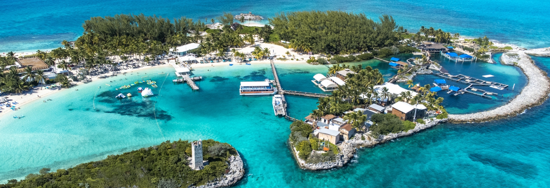 Aerial view of Blue Lagoon Island in the Bahamas featuring crystal clear turquoise water, white sand beaches, palm trees, water activities, docks, and tropical resort amenities