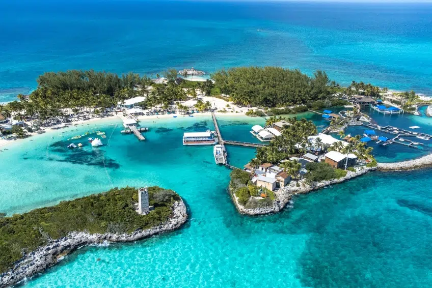 Stunning aerial view of Blue Lagoon Island in the Bahamas with turquoise Caribbean lagoons, white sandy beaches, palm tree groves, water sports equipment, and private island resort facilities