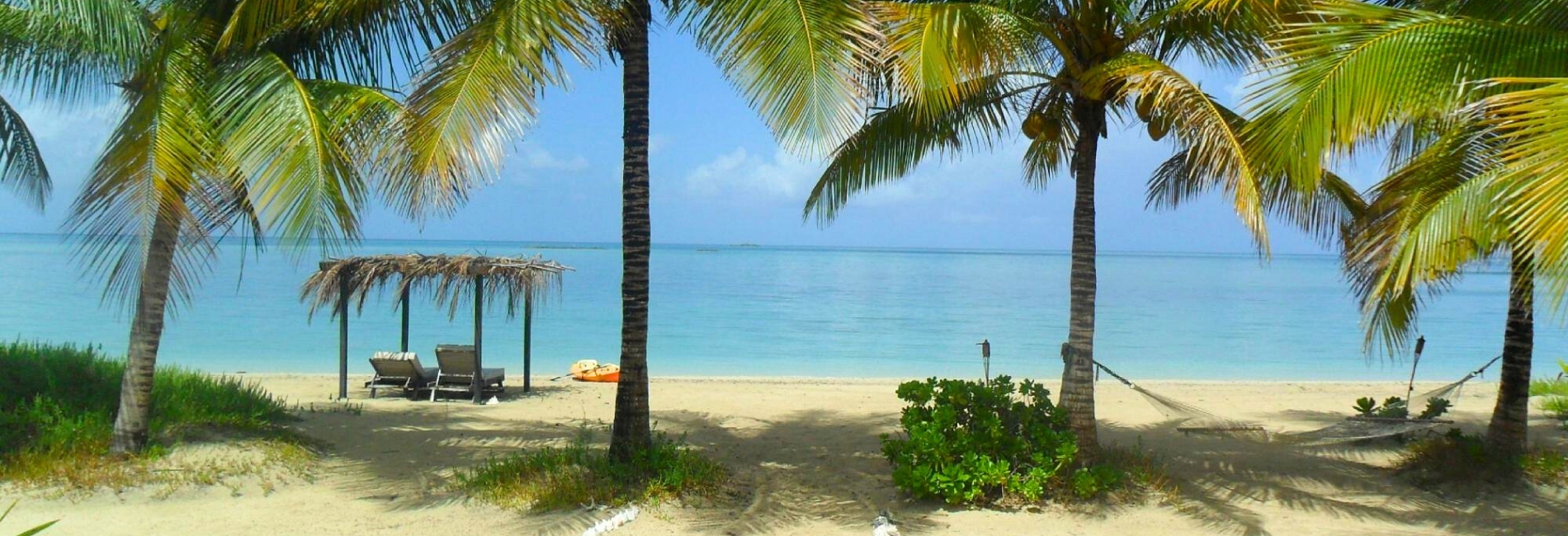 Tranquil beach at Kamalame Cay all-inclusive resort in the Bahamas with palm trees, hammock, thatched palapa, lounge chairs, kayak, and turquoise water