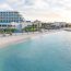 Panoramic view of luxury beachfront resort in the Bahamas featuring white sand beach, turquoise Caribbean water, palm trees, modern hotel buildings, and golden sunset light