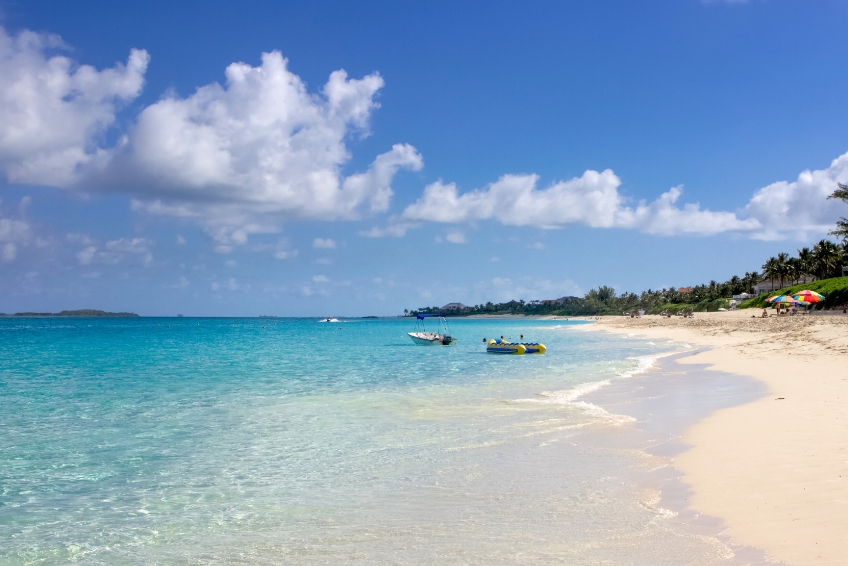 Scenic Paradise Beach in Nassau, Bahamas with turquoise Caribbean water, white sandy shore, palm trees lining the beach, colorful umbrellas, and distant islands