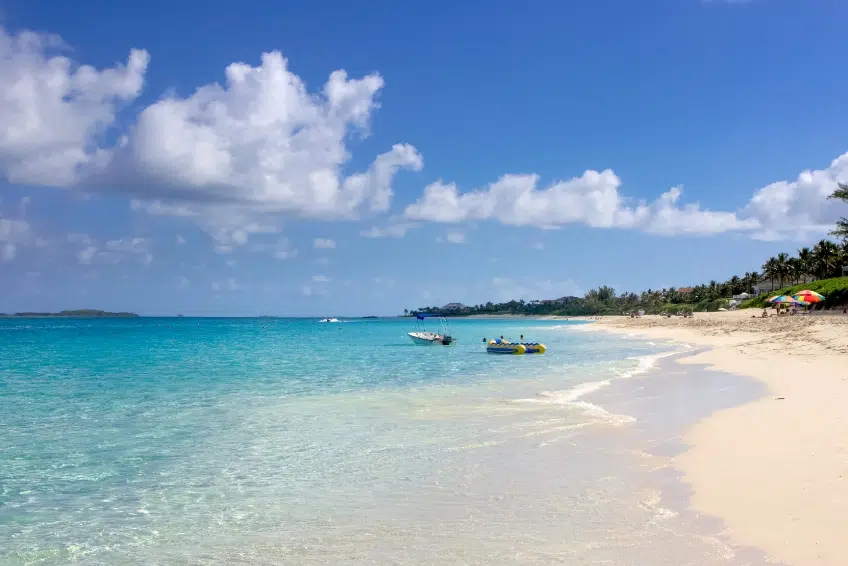 Scenic Paradise Beach in Nassau, Bahamas with turquoise Caribbean water, white sandy shore, palm trees lining the beach, colorful umbrellas, and distant islands