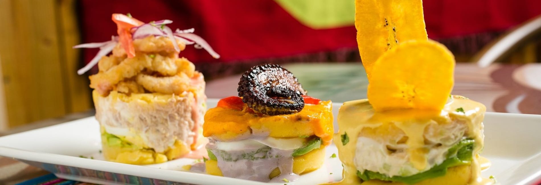 Colorful dishes at Asi es mi Peru restaurant in Aruba featuring ceviche towers with fresh fish, causa, plantain chips, and traditional Peruvian presentations