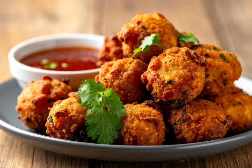 Crispy golden conch fritters, a traditional Bahamian appetizer, garnished with cilantro and served with tangy dipping sauce