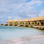 Luxury private cabanas at Renaissance Wind Creek Aruba Resort lined along the waterfront with thatched palapa roofs, outdoor loungers, water slide, and crystal clear turquoise water