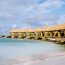 Luxury private cabanas at Renaissance Wind Creek Aruba Resort lined along the waterfront with thatched palapa roofs, outdoor loungers, water slide, and crystal clear turquoise water