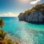 Beautiful Cayman Islands coastline featuring white limestone cliffs covered in tropical foliage, swaying palm trees, sparkling turquoise water, and bright blue sky