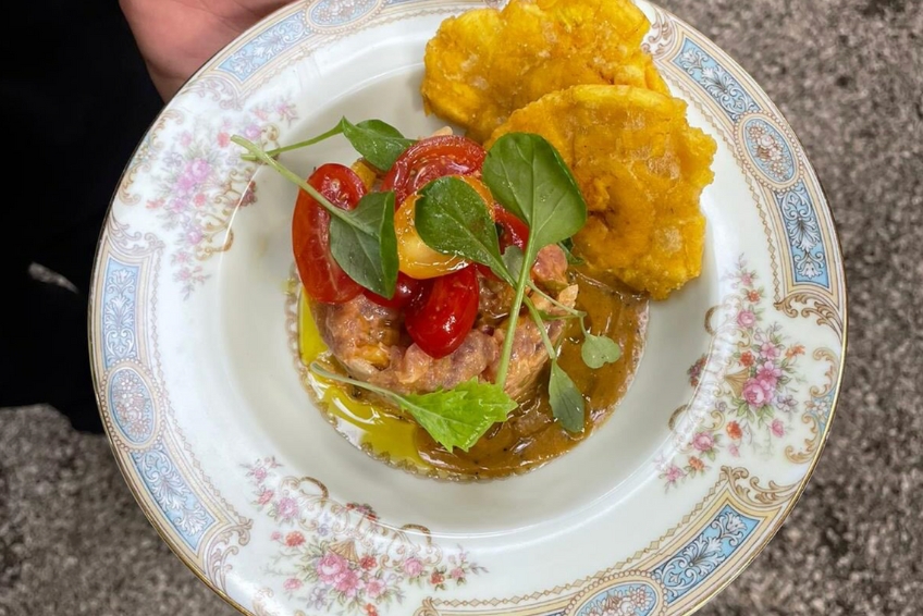 Beautifully plated pork at Cocina Al Fondo in Puerto Rico with crispy tostones plantains, roasted tomatoes, microgreens garnish, and aromatic sauce served on elegant floral china