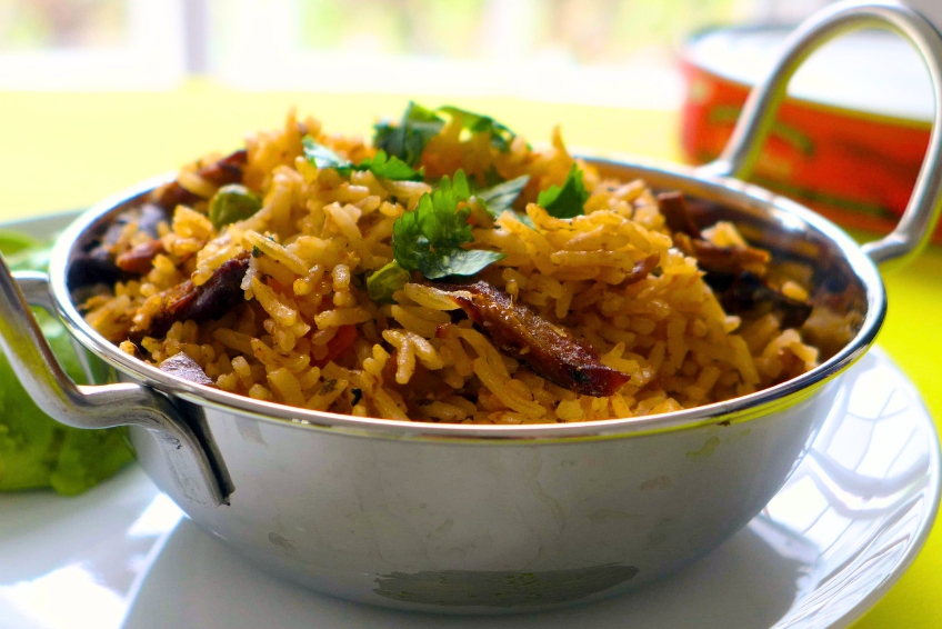 Traditional Dominican Locrio featuring yellow seasoned rice cooked with meat, garnished with fresh cilantro, served in a stainless steel bowl