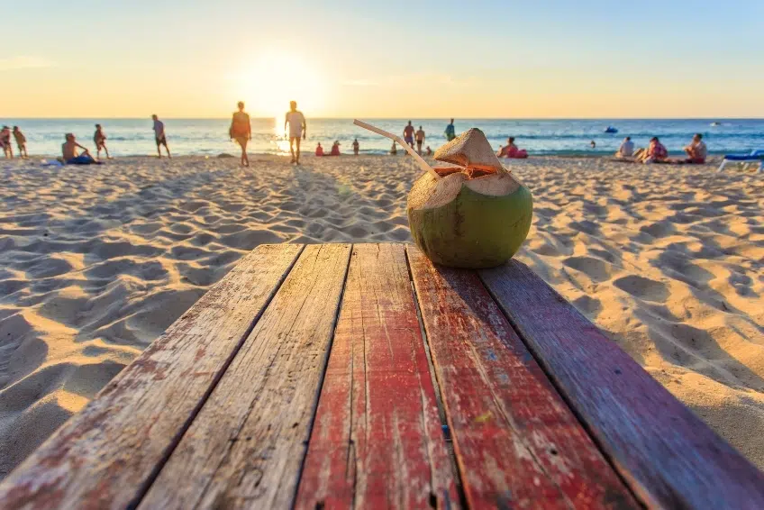 Tropical coconut beverage served at budget-friendly beachside spot on Reduit Beach St. Lucia during sunset with people relaxing on golden sand and turquoise ocean