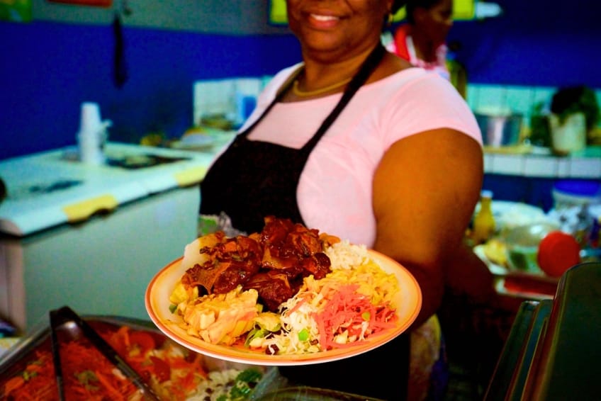 Budget-friendly Caribbean meal from Castries Market in St. Lucia with rice, braised meat, pink coleslaw, and pasta salad held on colorful plate at market vendor