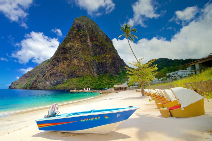 Iconic St. Lucia beach at Sugar Beach featuring towering Piton mountain covered in lush green vegetation, pristine white sand, crystal clear turquoise water, resort amenities, and tropical palm trees