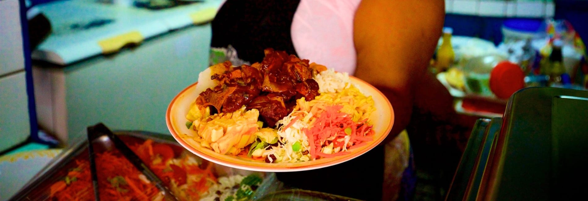 Traditional St. Lucian plate from Castries Market featuring rice, stewed meat, coleslaw, and macaroni salad served on orange plate at affordable local food stall
