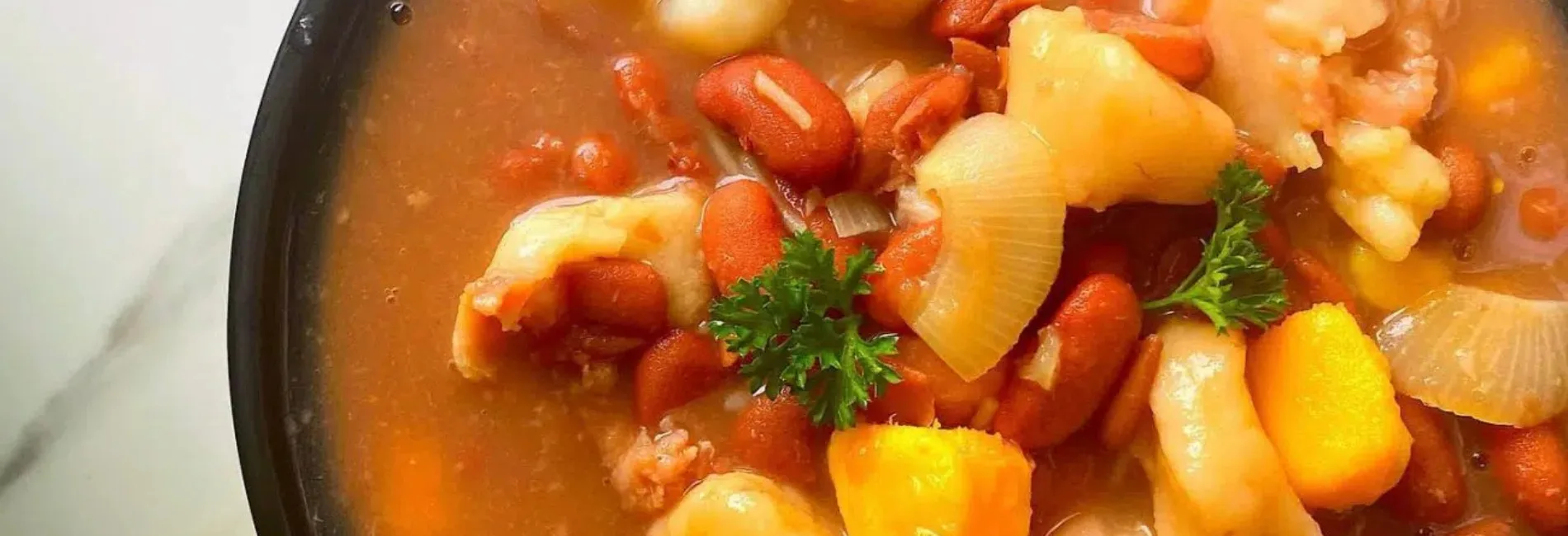 St. Lucia Budget Friendly Restaurants Caribbean Soup Vegetables Traditional Caribbean vegetable soup served at affordable St. Lucia restaurant featuring carrots, potatoes, and fresh parsley in savory broth in black bowl